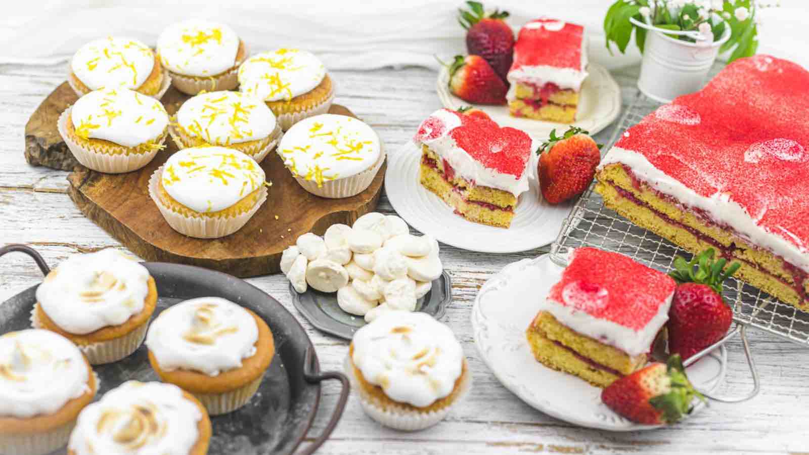 A variety of cakes and cupcakes on a wooden table.