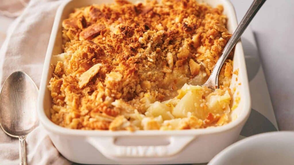 Pineapple casserole in a casserole dish with a serving spoon in it.