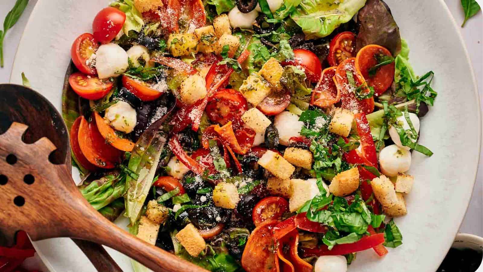 Homemade pizza salad in a serving bowl with wooden salad servers resting on top.