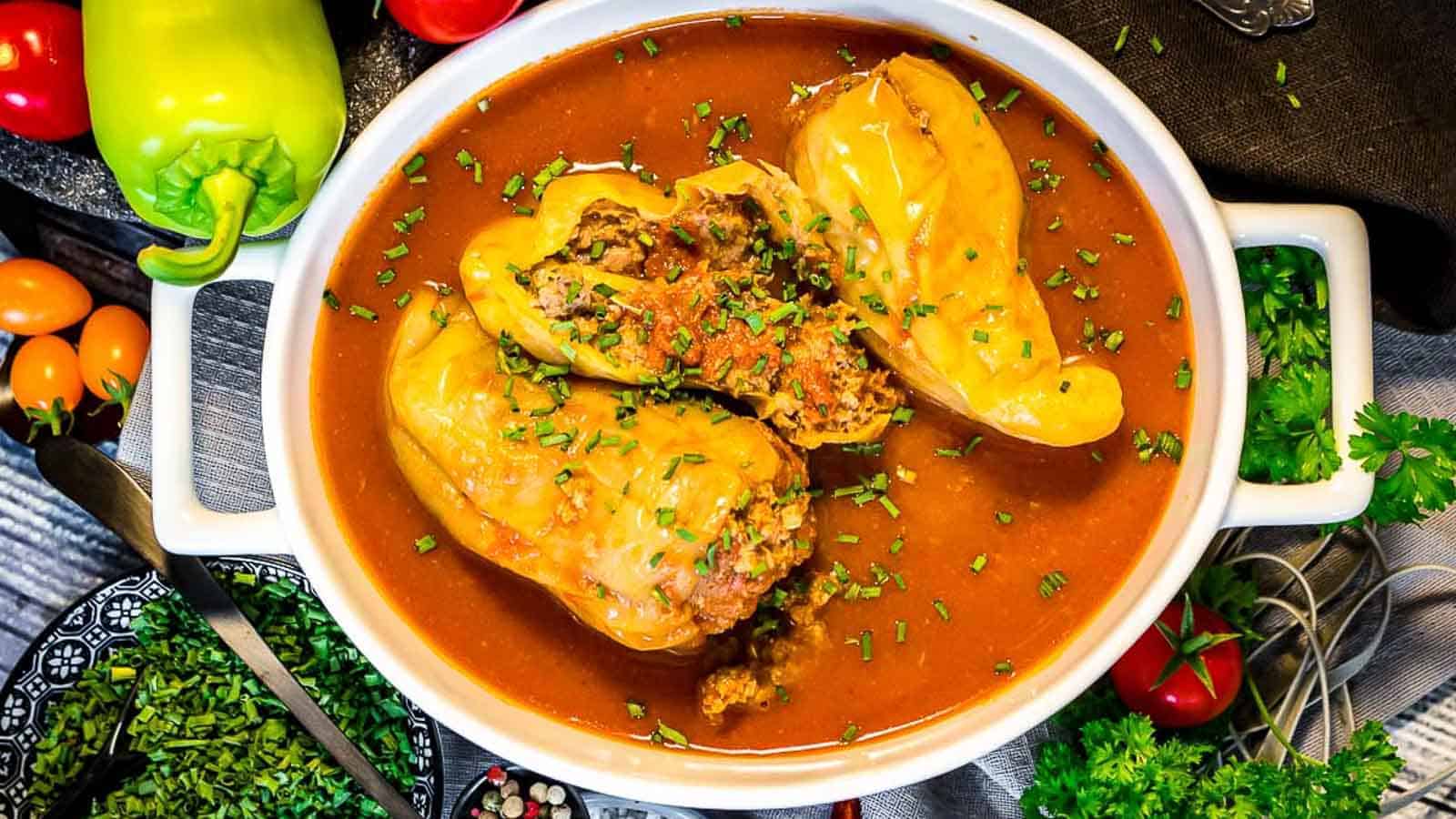 Stuffed peppers with tomato sauce inside a white dish. 