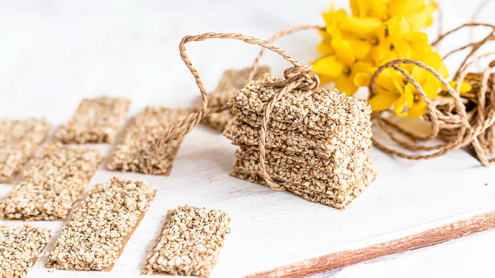 Sugar-Free Sesame Brittle Bars on a wooden board with yellow flower in the background. 