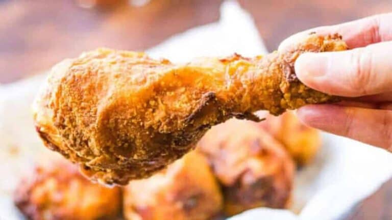 A hand holding a crispy fried chicken drumstick.