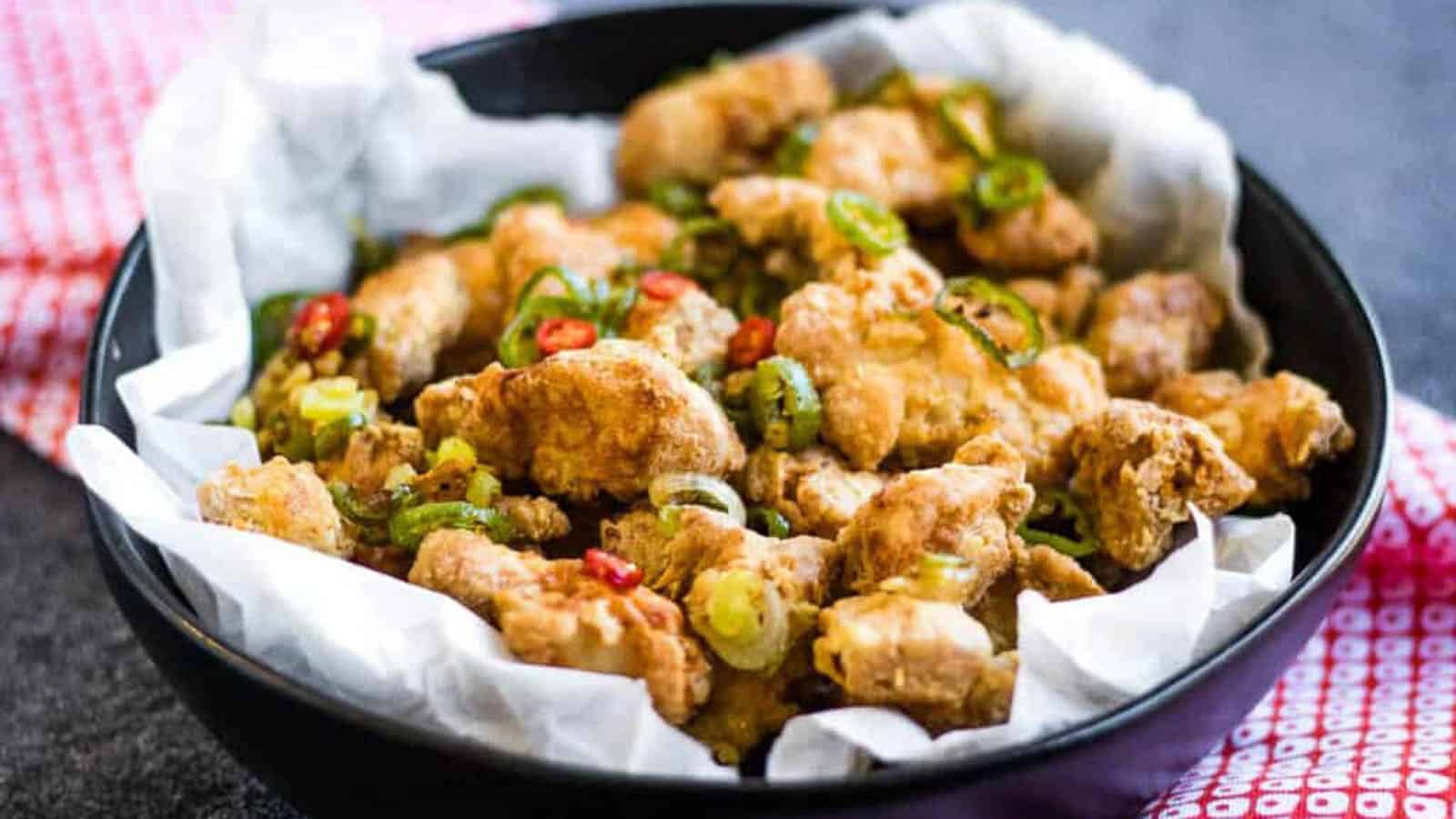 Fried salt and pepper chicken in a black bowl lined with parchment paper.