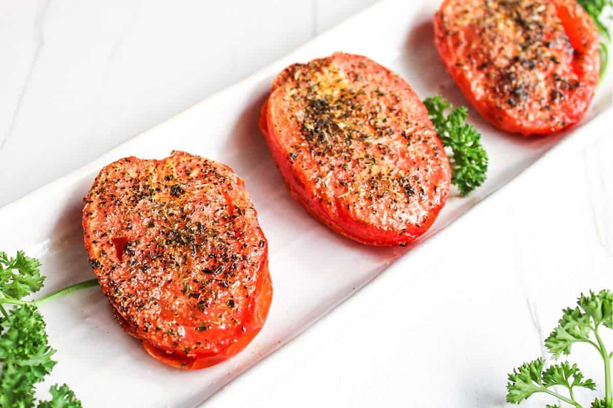 Three roasted tomatoes on a white plate with parsley.