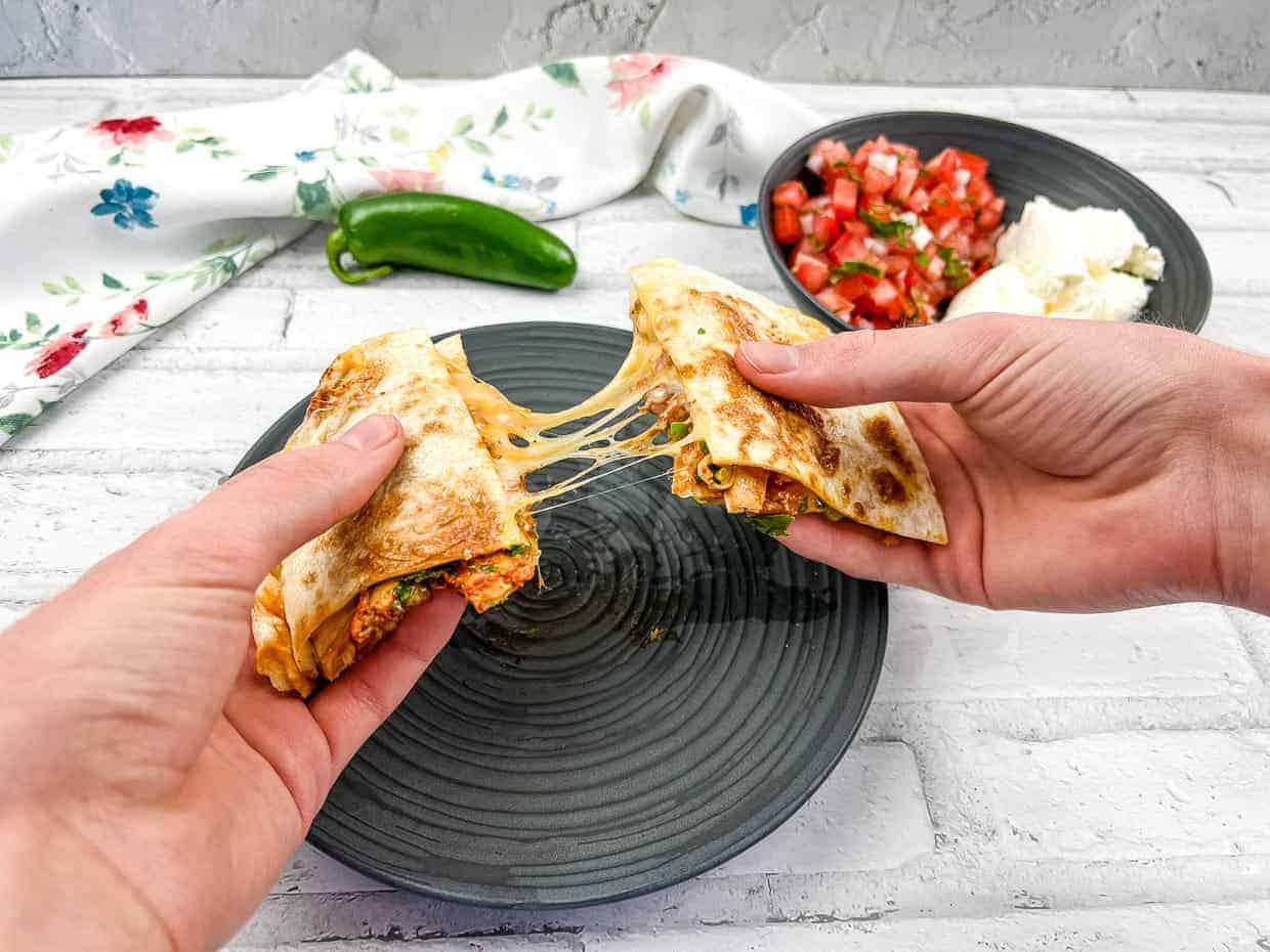 2 hands pulling a Chicken Al Pastor Quesadilla apart.