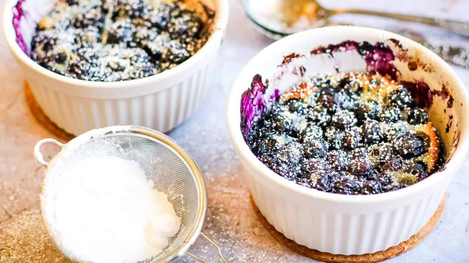 Low angle shot of 2 white ramekins filled with blueberry clafoutis.