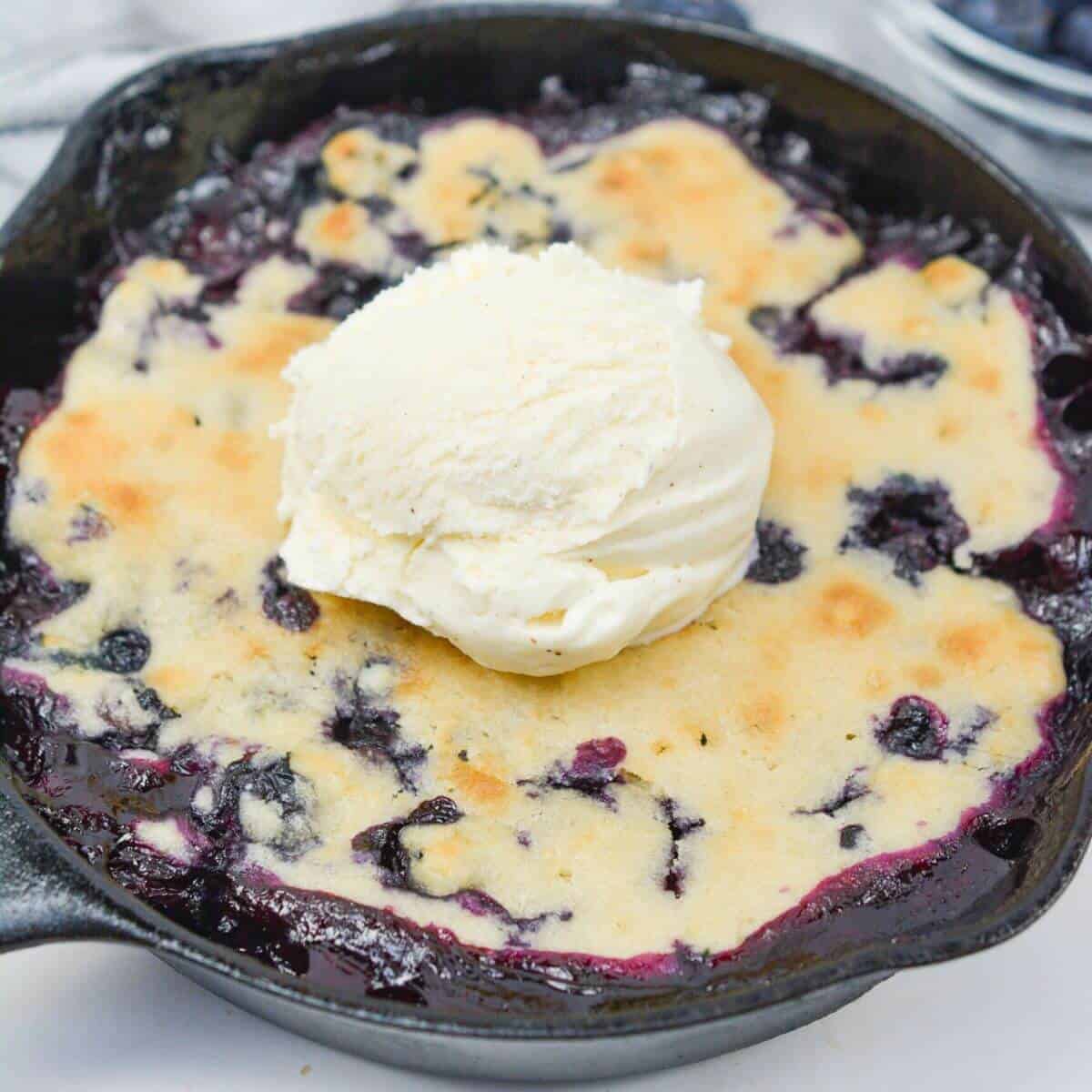 Mini blueberry cobbler in small cast iron skillet with scoop of vanilla ice cream.