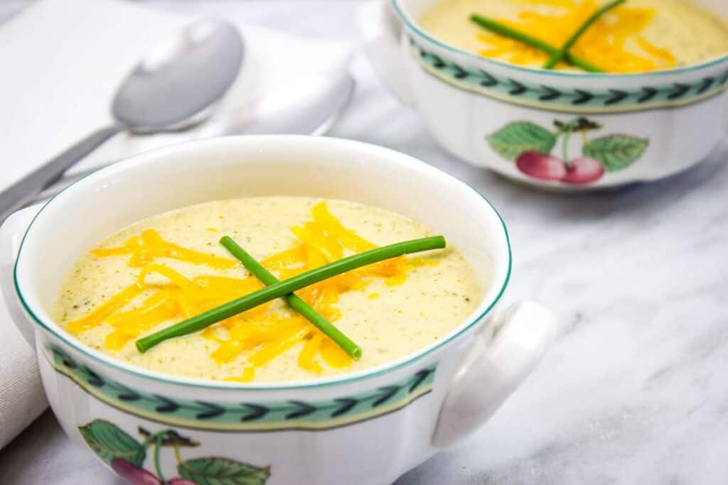 Broccoli Cheese Soup in two bowls with spoons nearby.