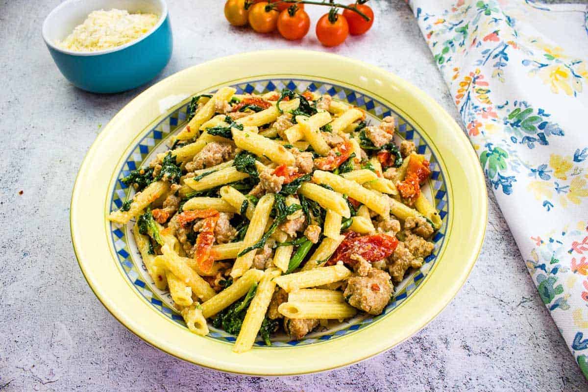 Broccoli Rabe and Sausage in a serving bowl with tomatoes in the background.