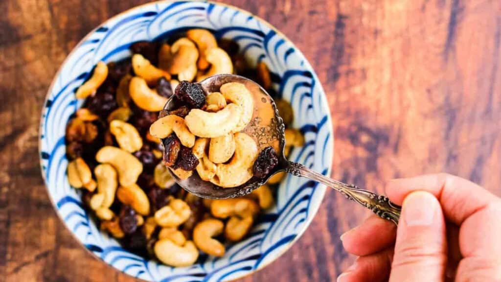 A hand is holding a bowl of cashew nuts.