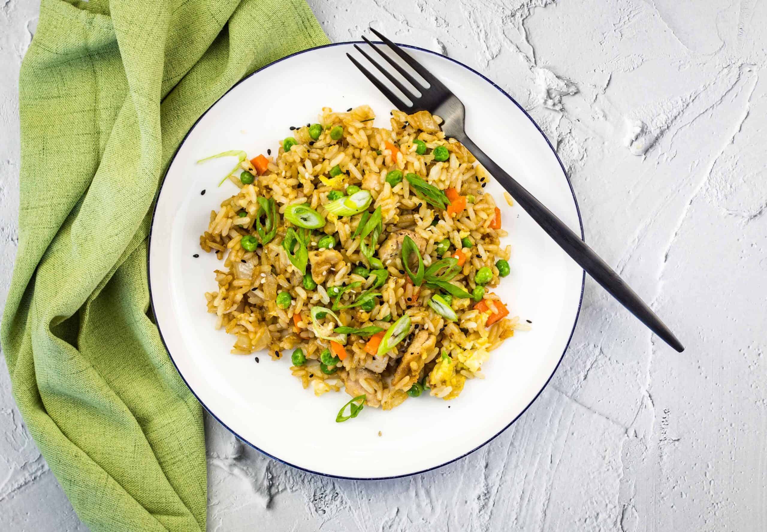 Chicken fried rice on a white plate with a green napkin.