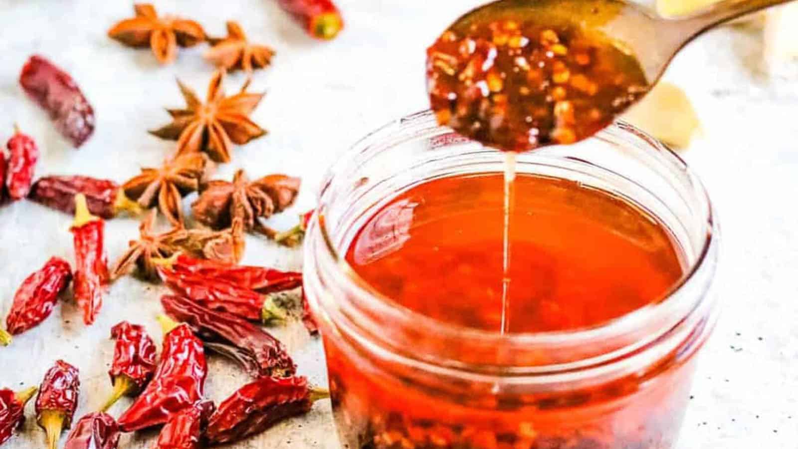 low angle shot of a jar of chili oil with a spoon lifting some of the oil out of the jar.