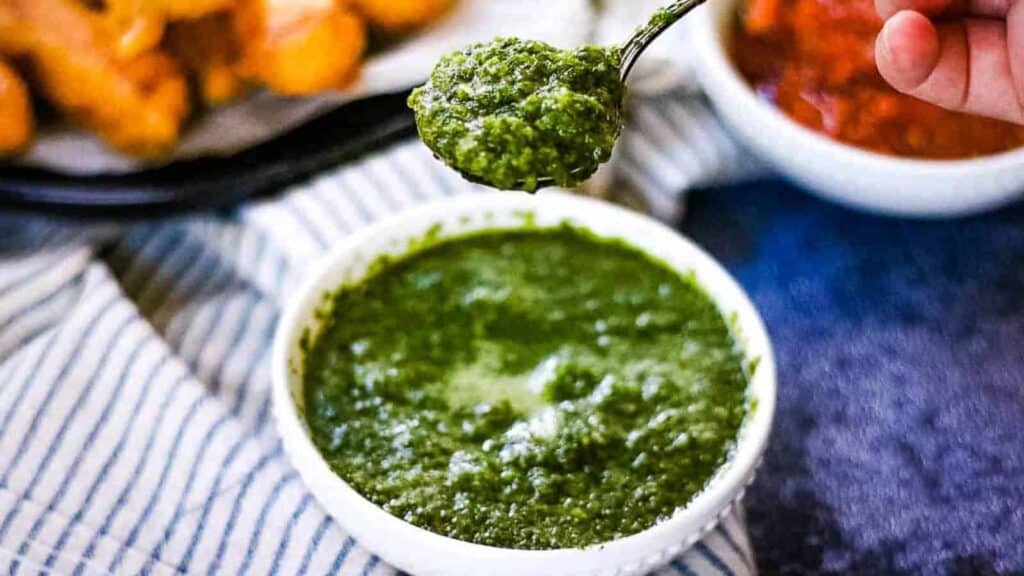 High angle shot of a bowl of cilantro mint chutney with a spoonful being lifted above the bowl.