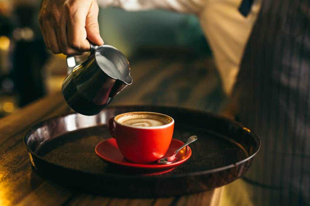 A barista pouring a cup of coffee on a tray.