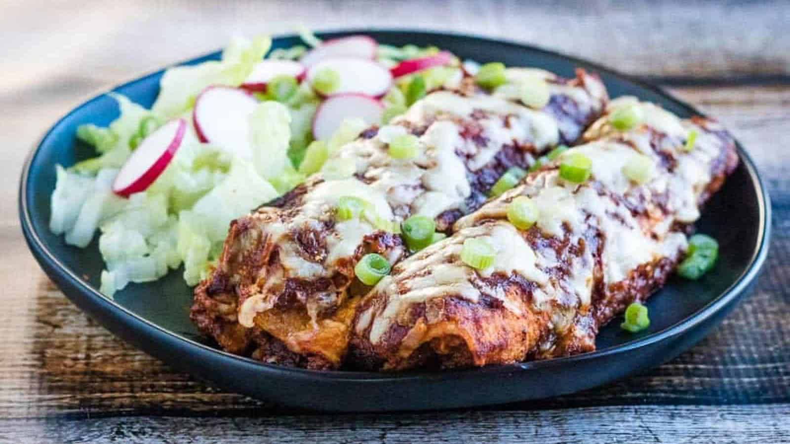 Low angle shot of chicken enchiladas on a plate with salad.