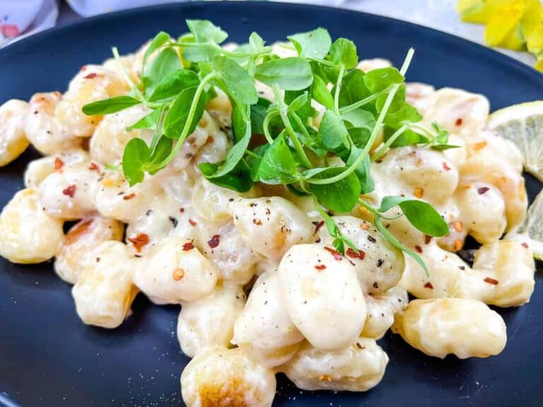 Gnocchi with lemon and parmesan on a black plate.