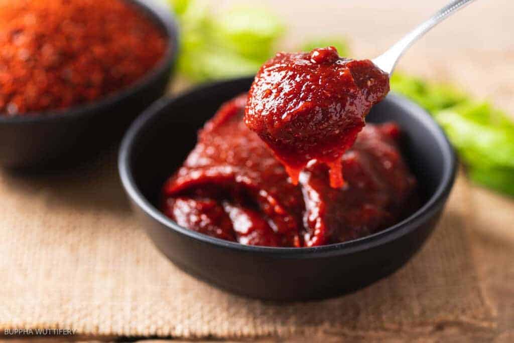 A spoon is pouring a red sauce into a bowl.