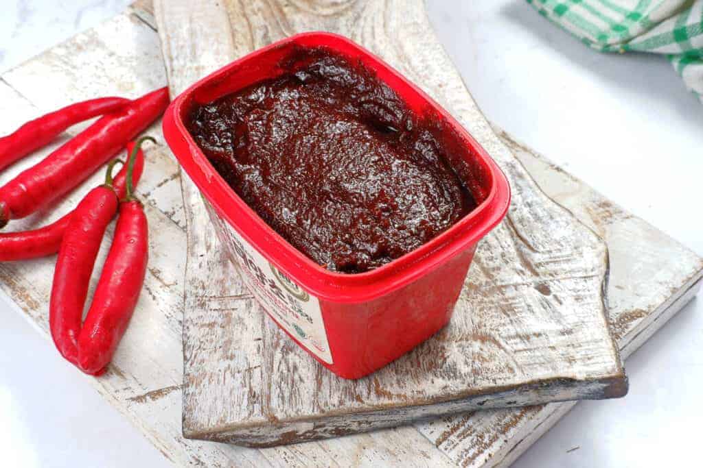 A container of chocolate sauce with red chilies on a cutting board.