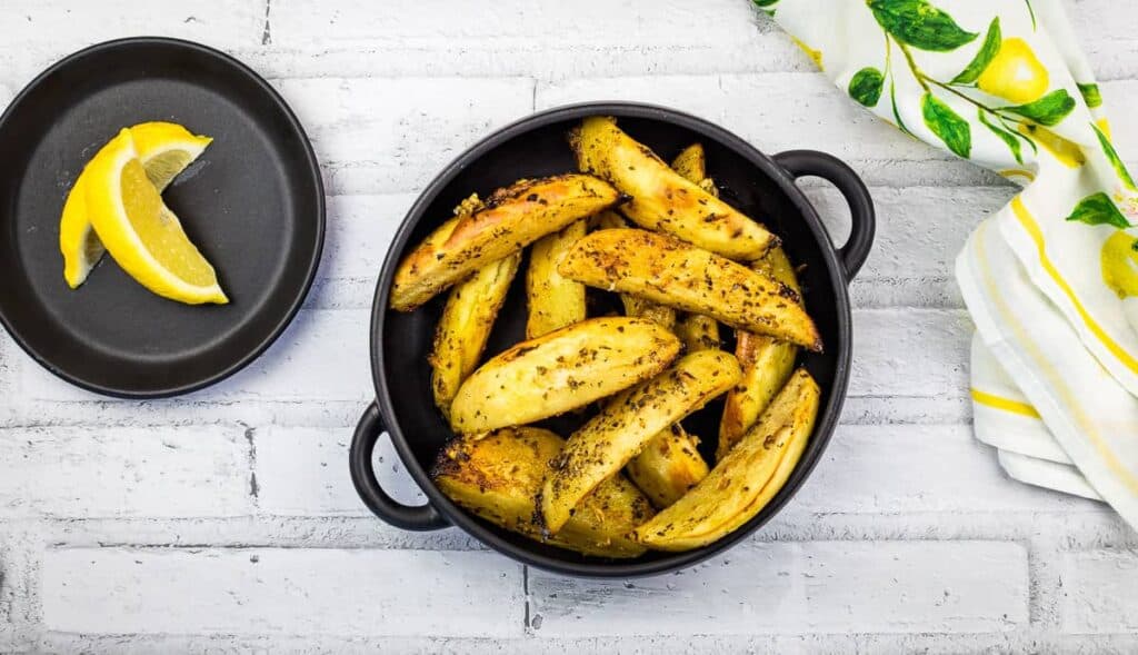 Greek Lemon Garlic Potatoes in a black dish with lemon in the background.