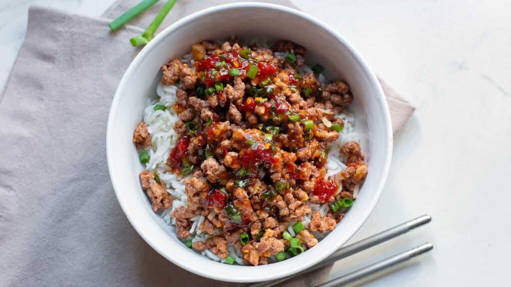 A white bowl with rice and hoisin ground beef and chopsticks on the side.