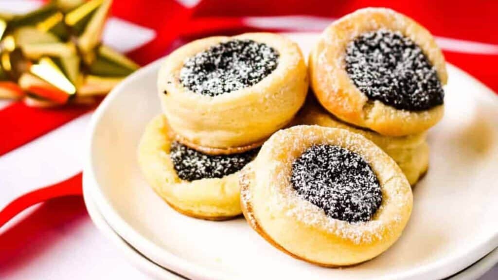 Several poppy seed filled kolacky on a white plate with red and gold ribbons in the background.