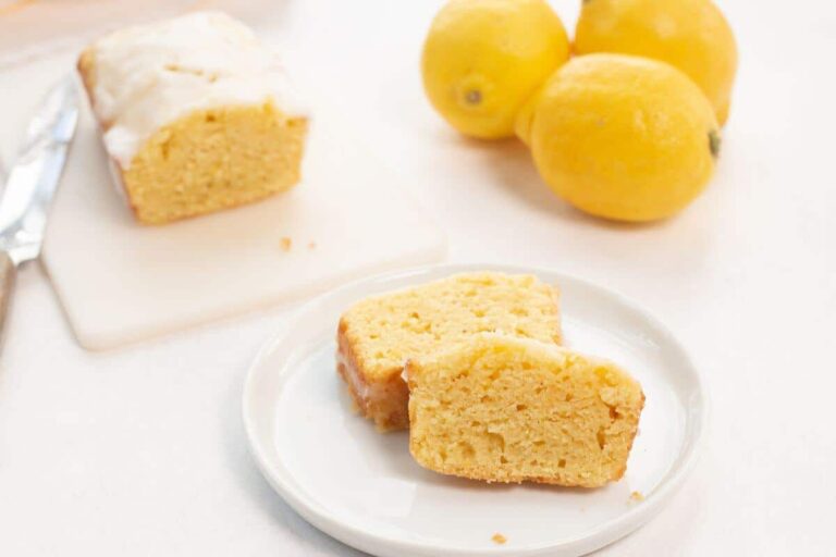 Lemon loaf on white cutting board with a cut slice.