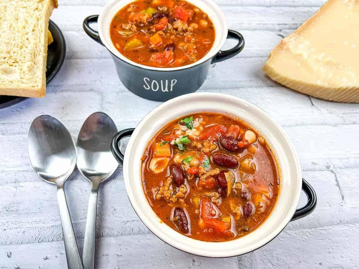 Two bowls of soup on a counter with bread nearby.