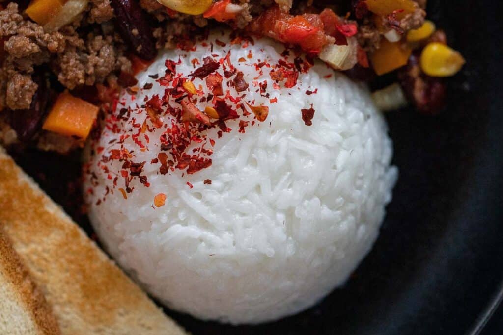 A bowl of rice with meat and vegetables on top.