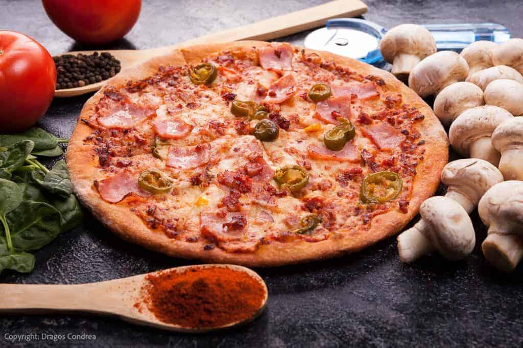 A pizza with mushrooms, tomatoes and olives on a black background.