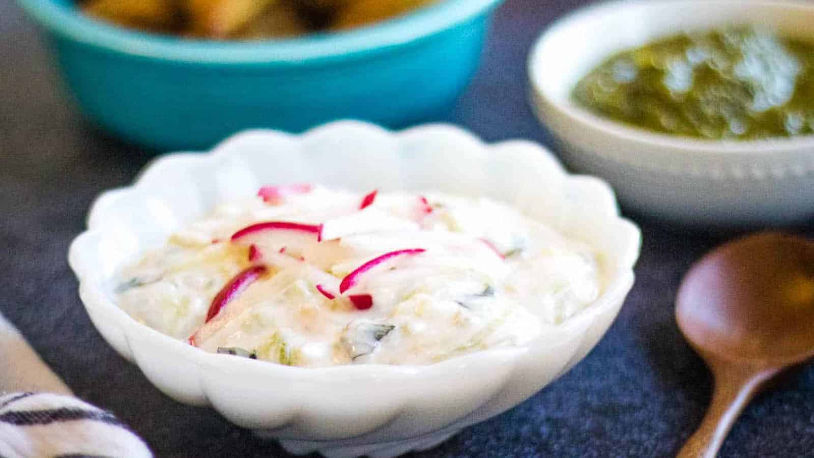 A low angle shot of a bowl of cucumber raita with radishes on top.