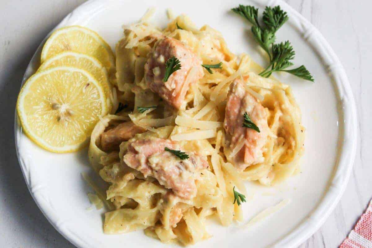 Salmon pasta Alfredo served on a white plate with lemon.