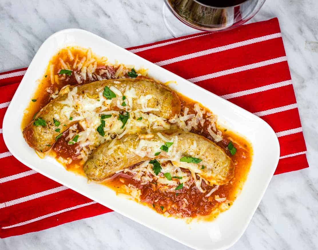 Sausage Parmigiana on a white plate with a red napkin and a glass of wine.