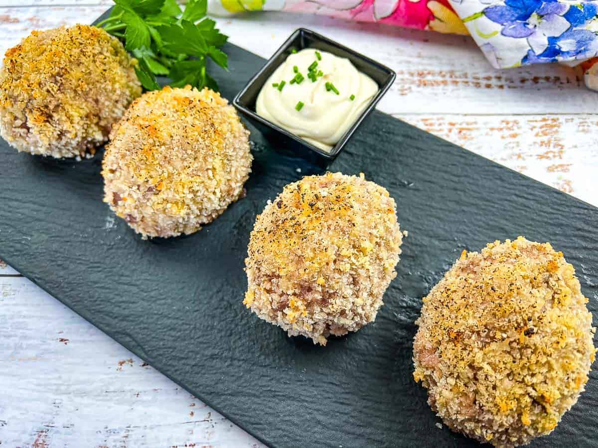 Scotch Eggs on a black plate.
