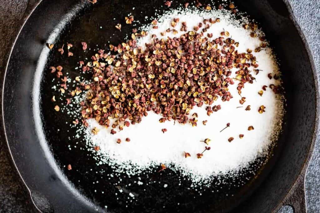 A frying pan with salt and szechuan peppercorns in it.