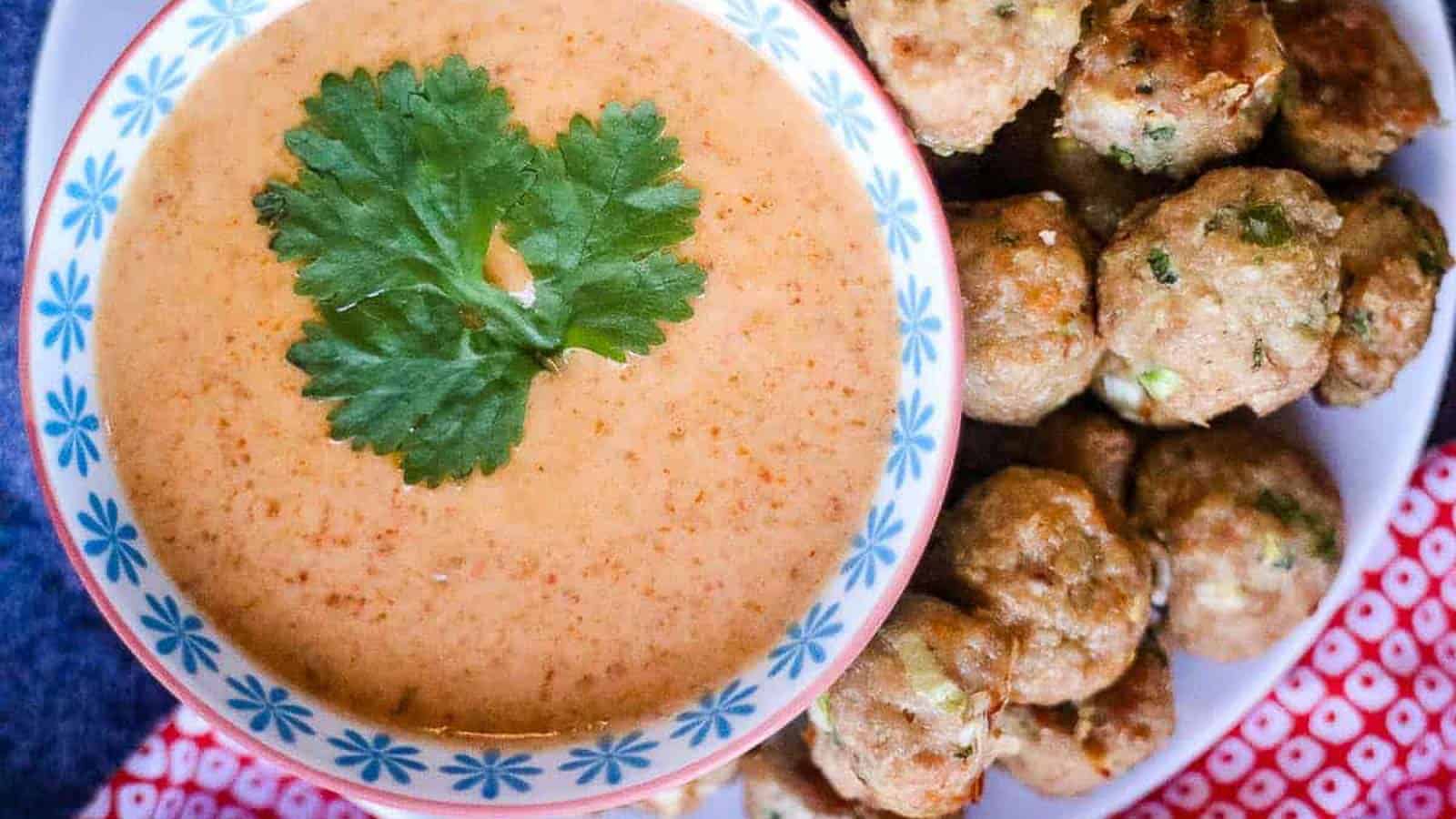 Overhead shot of a bowl of thai red curry sauce with a cilantro leaf on top.