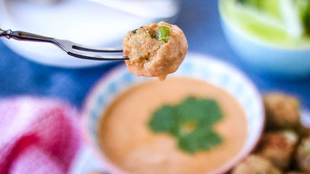 A fork is holding a bowl of meatballs with sauce.