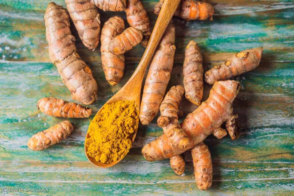 Tumeric powder and a wooden spoon on a wooden table.