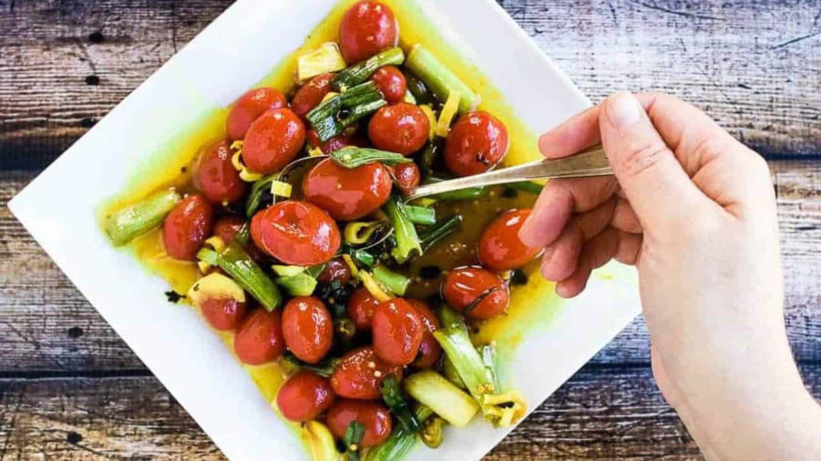 Quick Pickled Turmeric Tomatoes on a white plate with a hand lifting a spoonful.