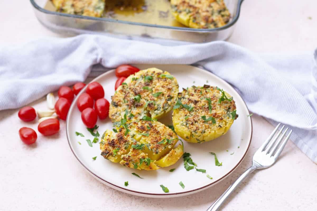 Three parmesan potatoes on a white plate with cherry tomatoes to the side.