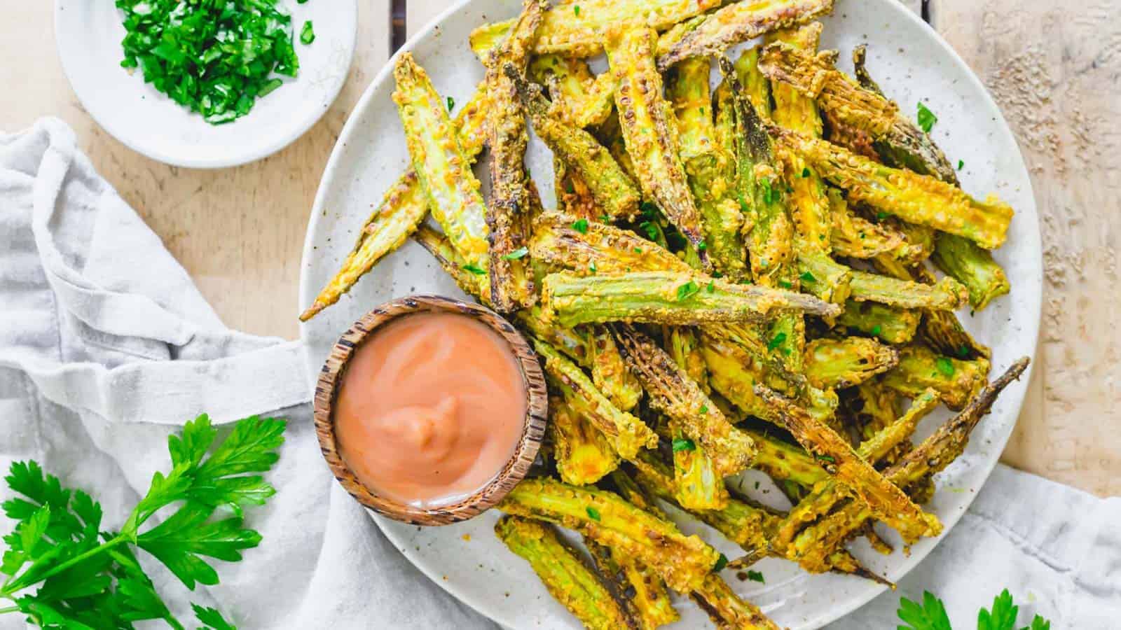 Spiced air fryer okra fries served with a yogurt dip on a plate with fresh parsley.