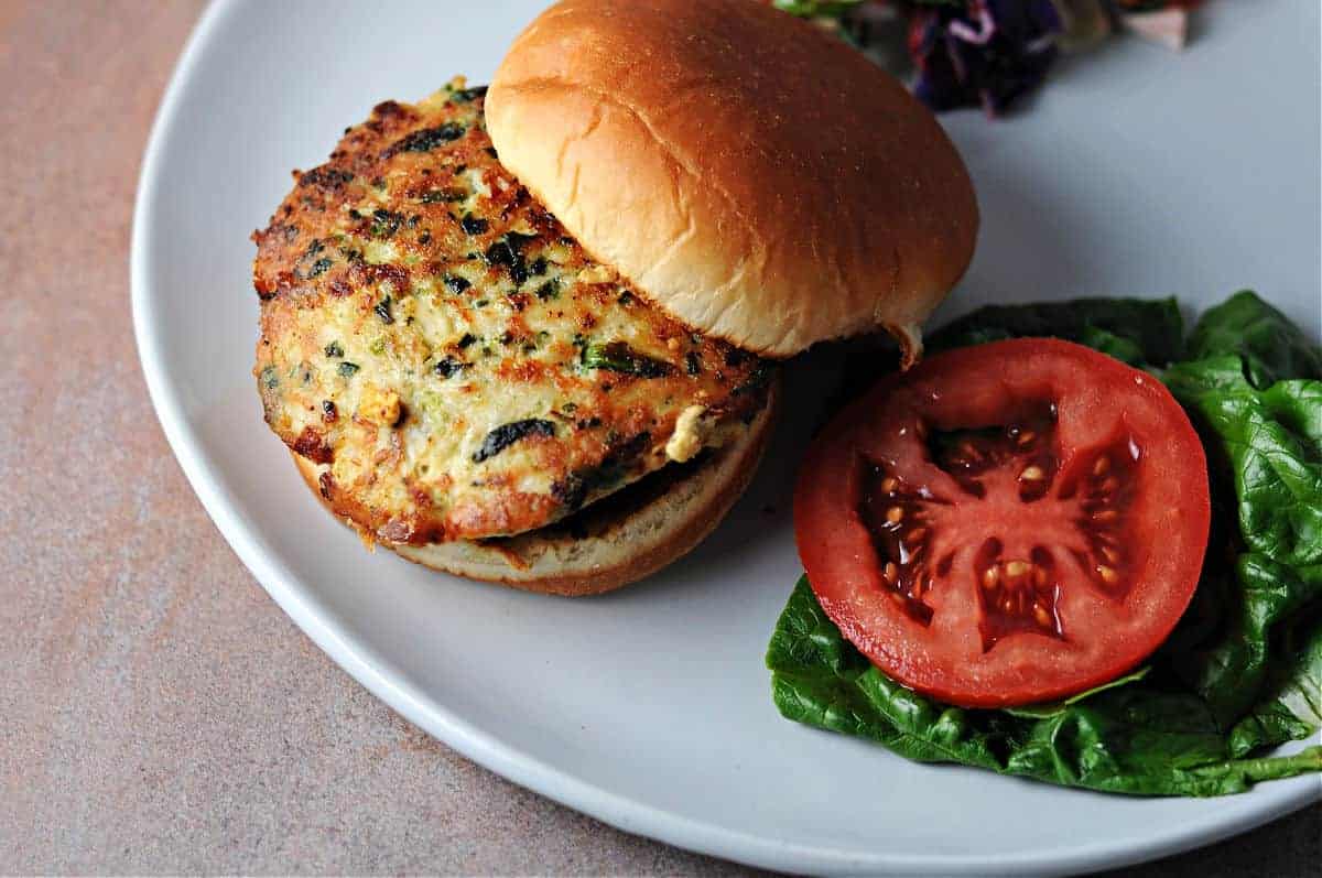 Chicken burger on a bun with lettuce and a tomato slice ready to add.