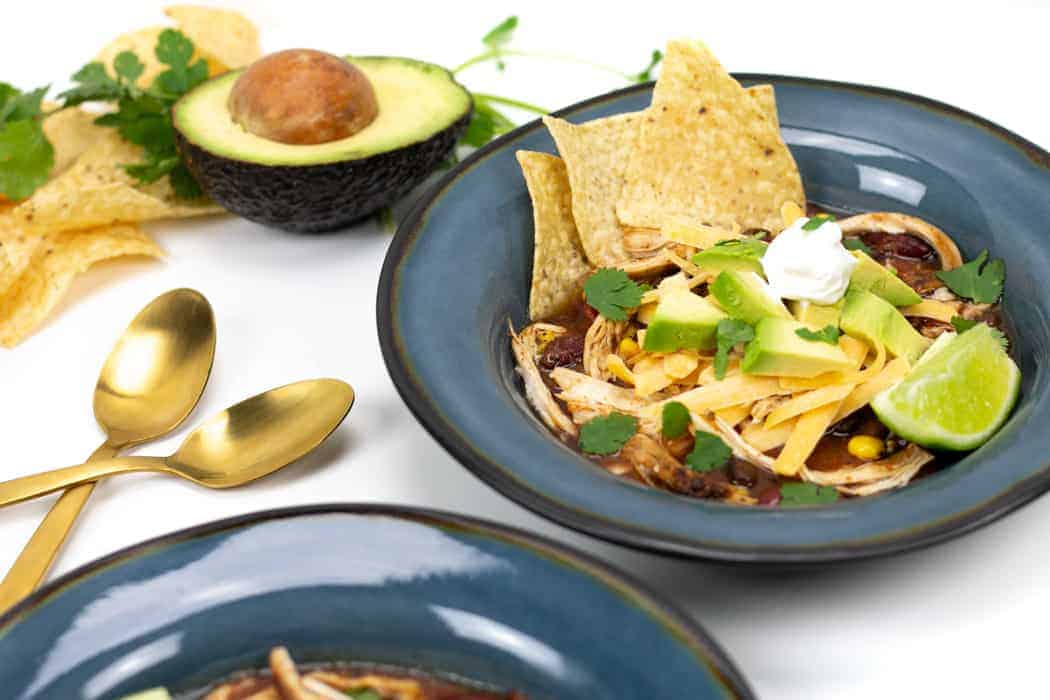 two blue bowls of chicken tortilla soup and spoons.