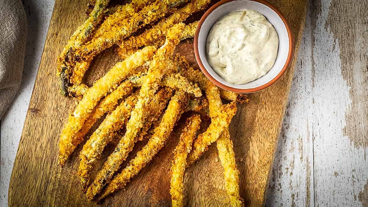 Top view of green bean fries on a cutting board with dipping sauce.