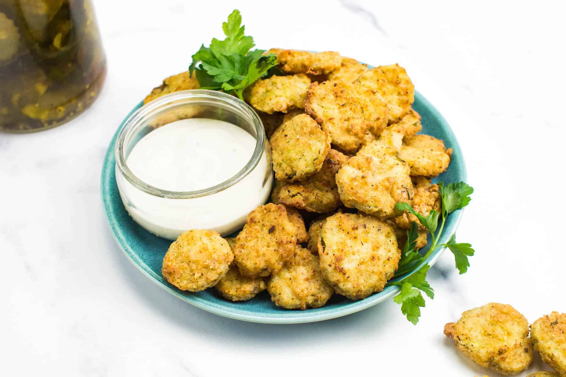 a blue plate with fried pickles and a glass container of ranch sauce.