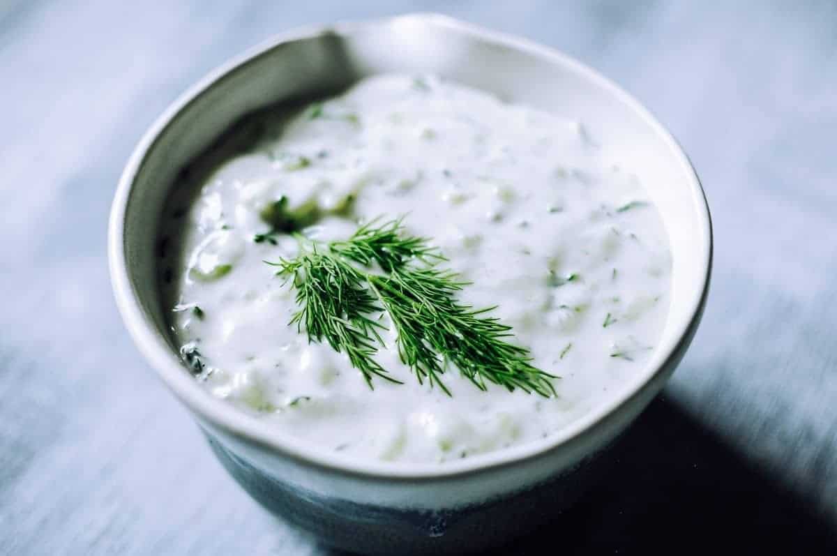 A small ceramic dish filled with a white sauce topped with fresh green herbs.