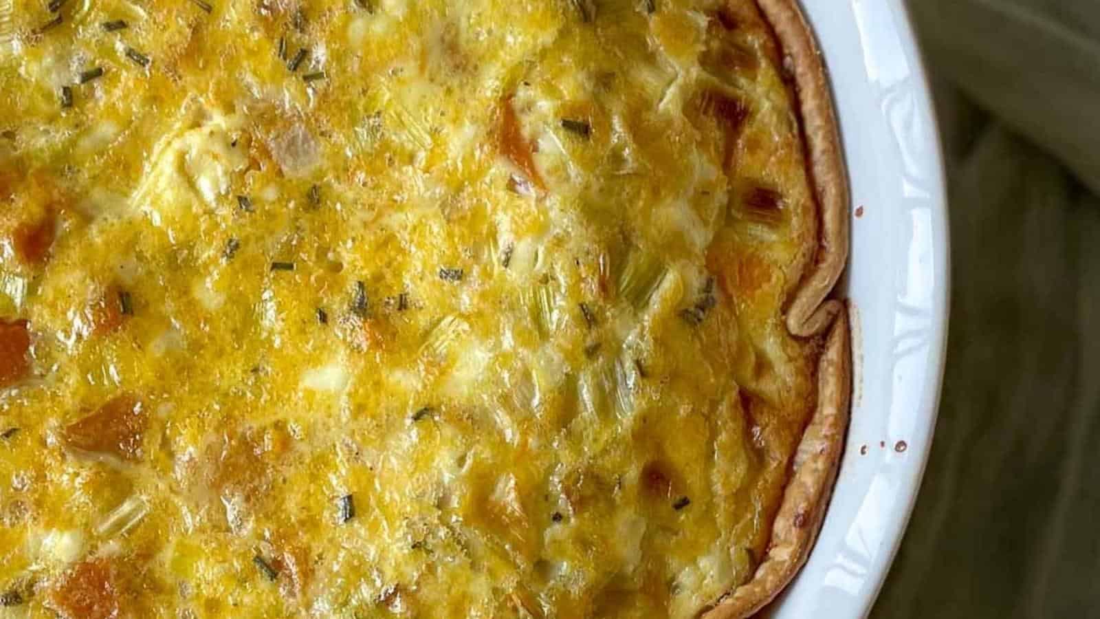 A quiche is sitting in a white dish on a table.