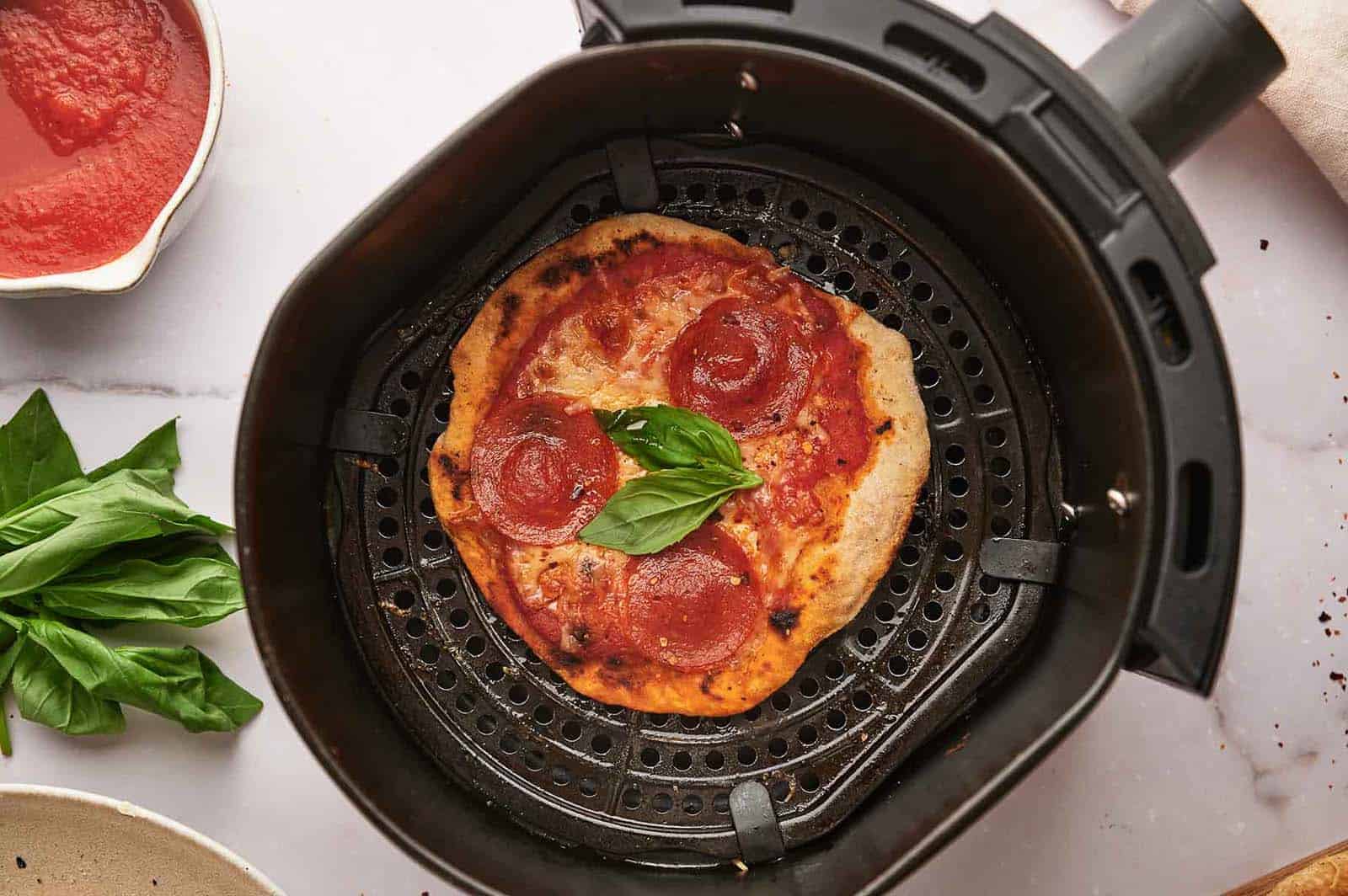 A tortilla pizza in an air fryer basket.