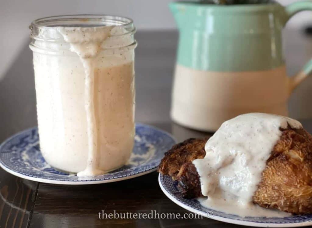 A jar of white bbq sauce with a drip and chicken covered in it on the side.