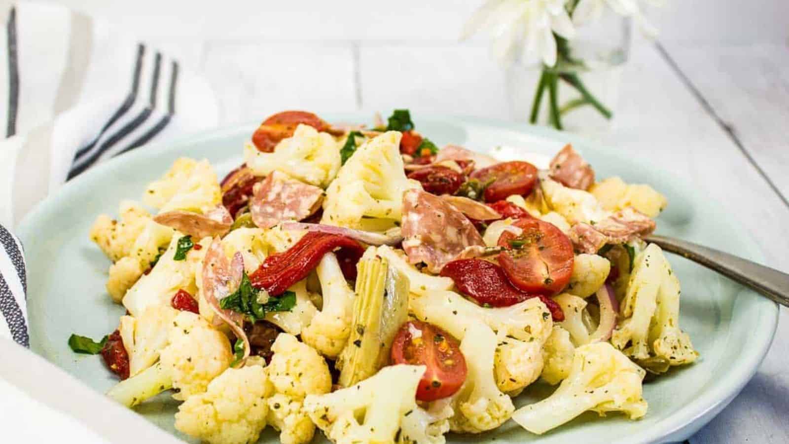 Low-carb Antipasto Salad on a round plate with daisies in the background.