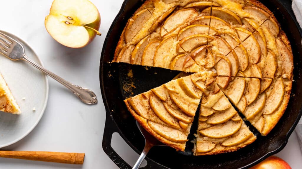 A slice of apple cake in a cast iron skillet.